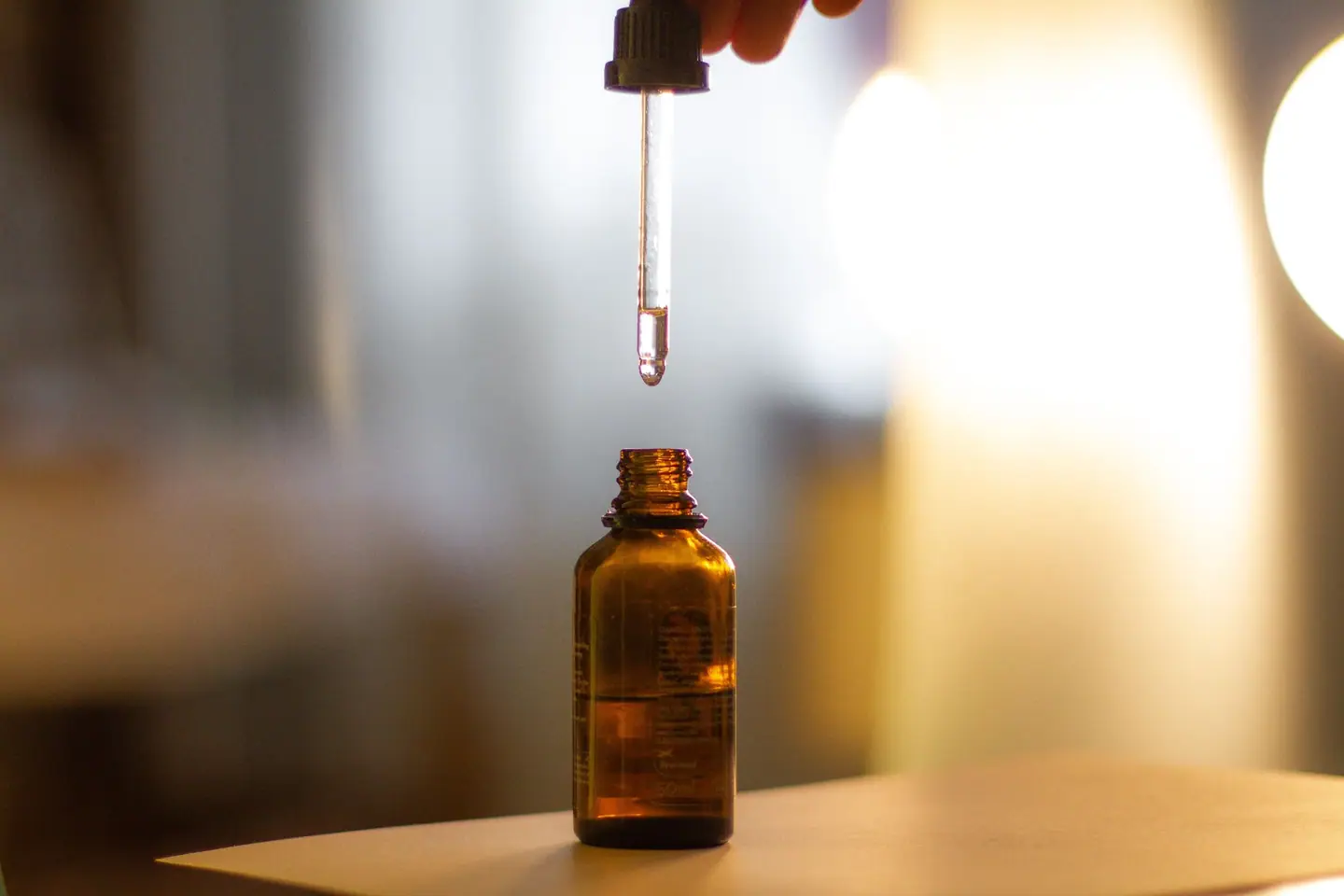 A dropper held above an amber glass dropper bottle in warm light